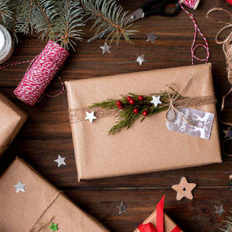 Spread the cost of Christmas with homemade gifts - Birds eye view of Christmas presents laid out on a wooden floor, wrapped up with brown paper, twine, fresh branches and dried fruit.