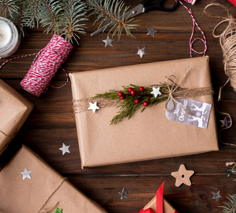Spread the cost of Christmas with homemade gifts - Birds eye view of Christmas presents laid out on a wooden floor, wrapped up with brown paper, twine, fresh branches and dried fruit.