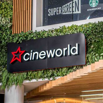 Black Cineworld sign hanging on wall with wooden cladding and green leafy decoration.