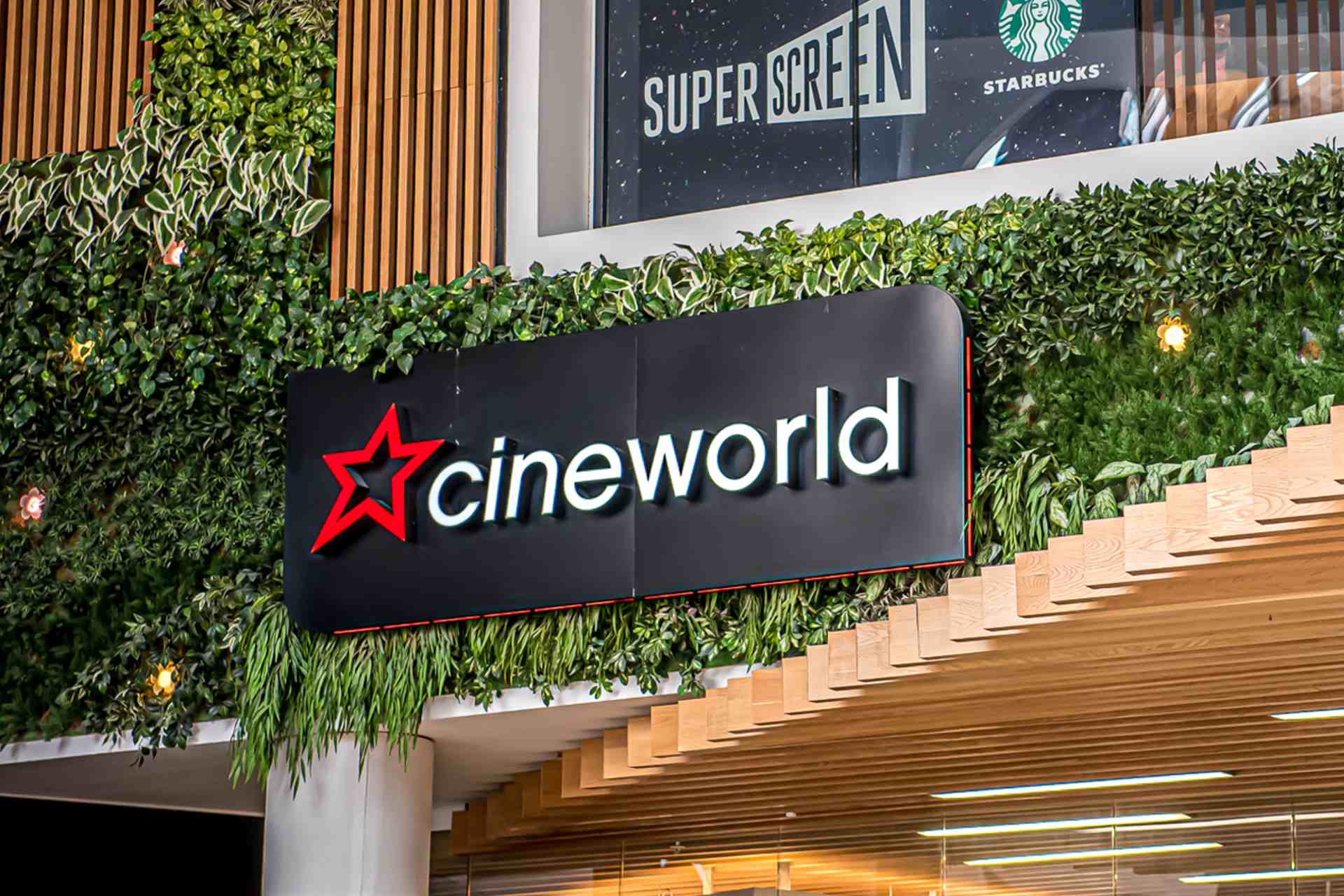 Black Cineworld sign hanging on wall with wooden cladding and green leafy decoration.
