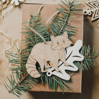 Eco friendly christmas - top down view of wooden raccoon bauble with pine needles and wooden snowflake baubles on a brown paper background