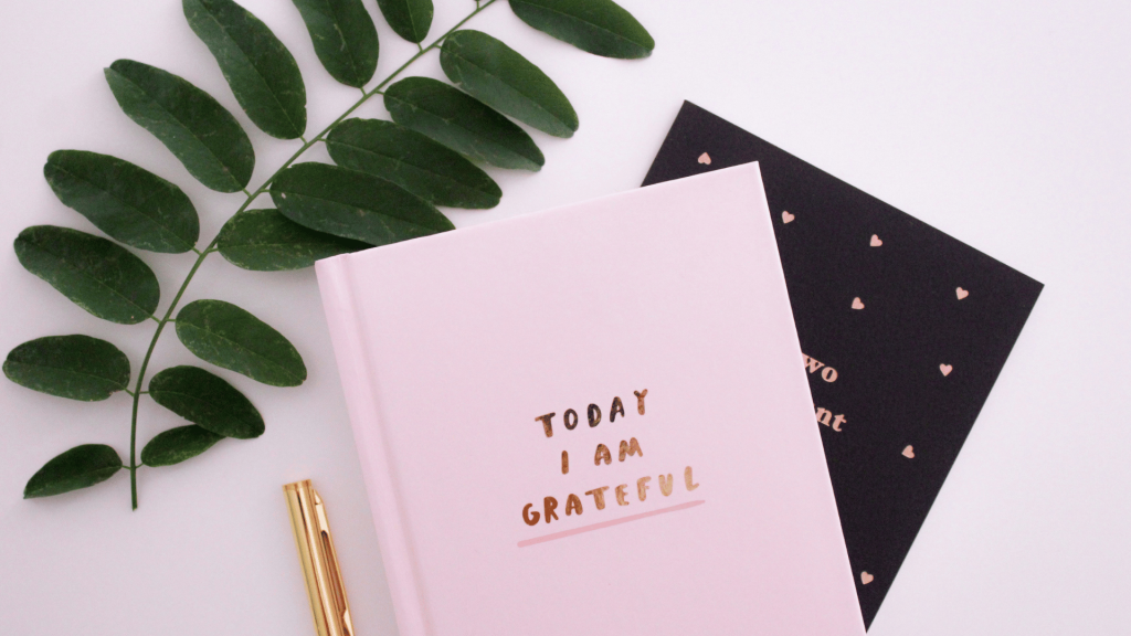 A journal with "Today I am Grateful" on the front next to a pen and a leaf.