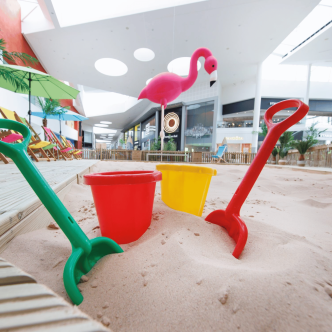 A flamingo in the background behind a sandy beach with buckets and spades.