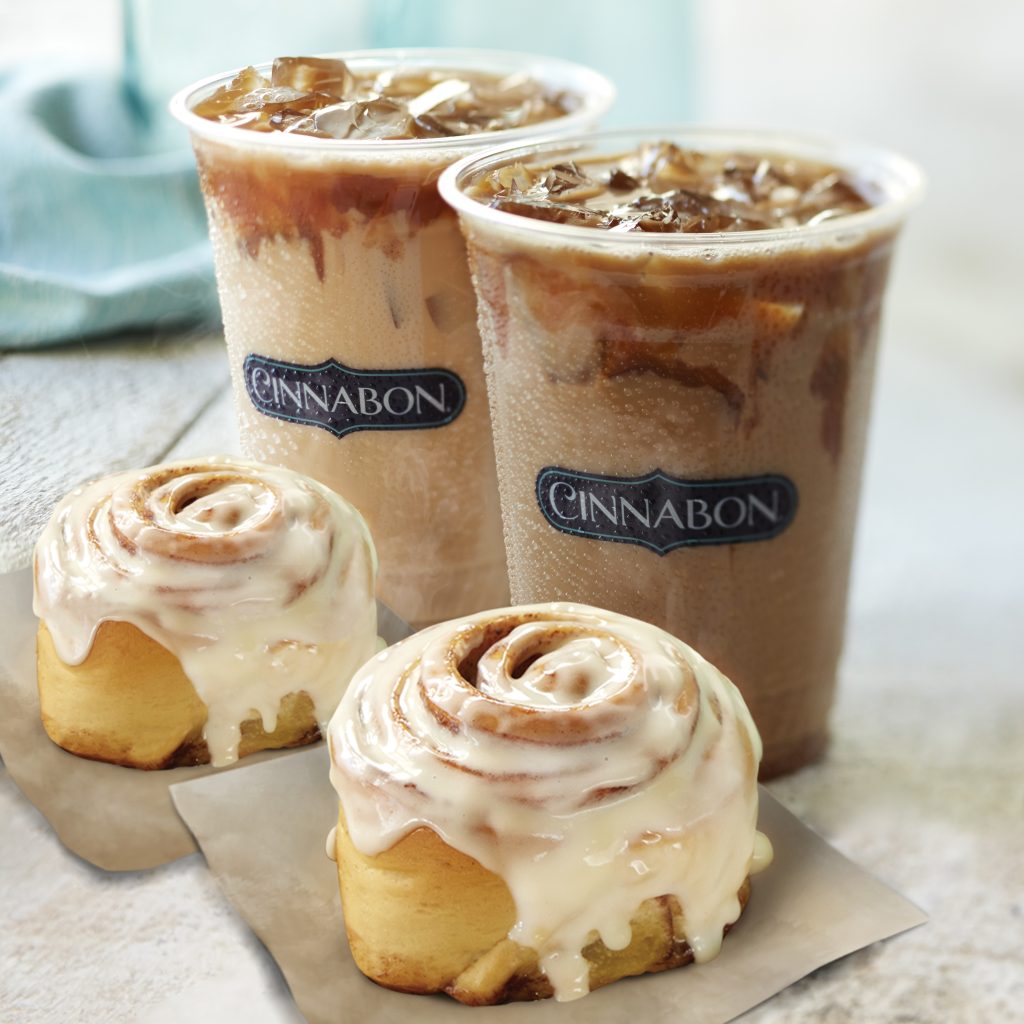 Two Cinnabon cinnamon rolls with two iced lattes.